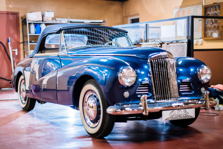 Vue d’ensemble du garage avec la voiture d’époque en préparation pour l’inauguration.