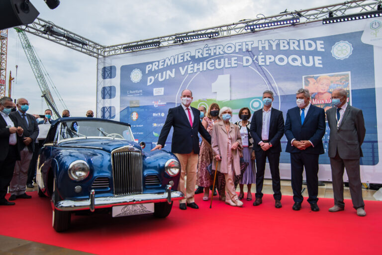 Le Prince Albert II de Monaco et Brigitte Auber posent devant la voiture rétrofitée, symbole d’innovation et d’élégance.