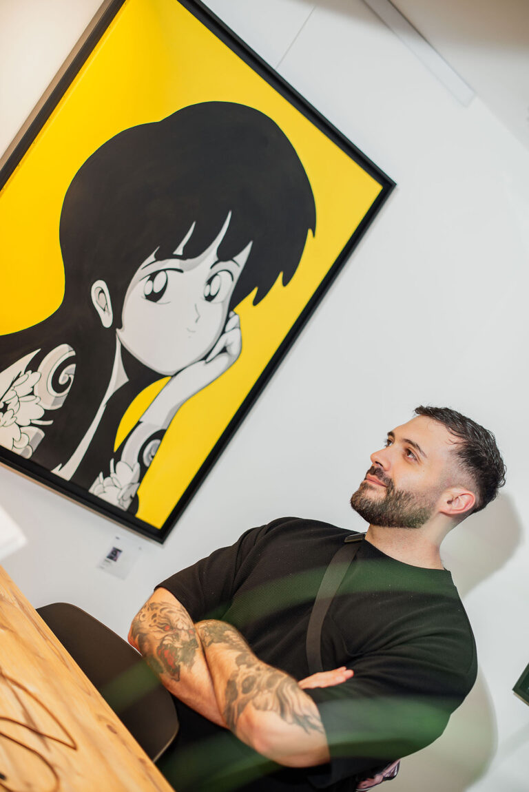 Un artiste contemporain pose aux côtés de son œuvre exposée.