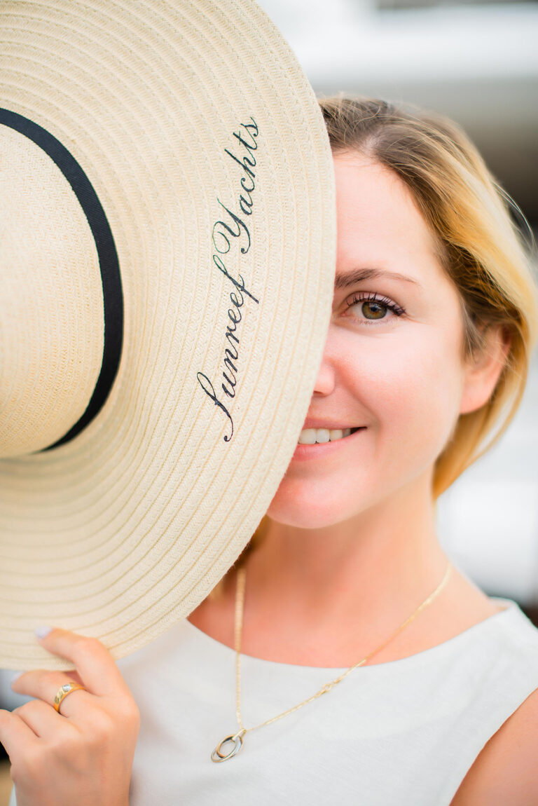 Portrait artistique d’une hôtesse cachant partiellement son visage derrière un chapeau de marque nautique.