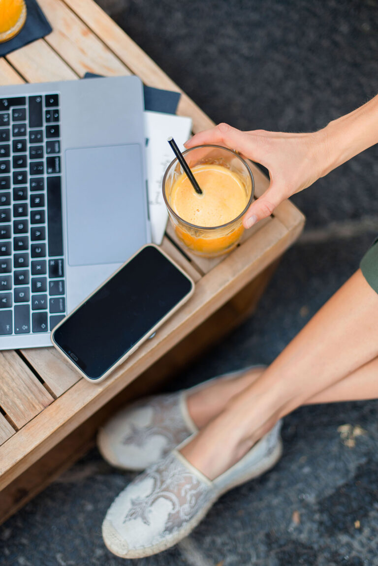 Outils de travail d’une nutritionniste : ordinateur, smartphone et jus de fruits sur une table de café.