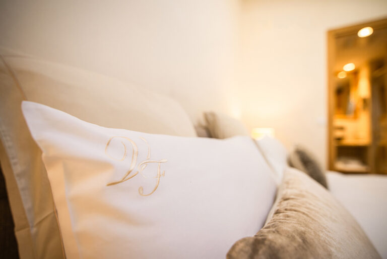 Détail d’un oreiller brodé sur un lit élégant, ambiance cosy et raffinée.