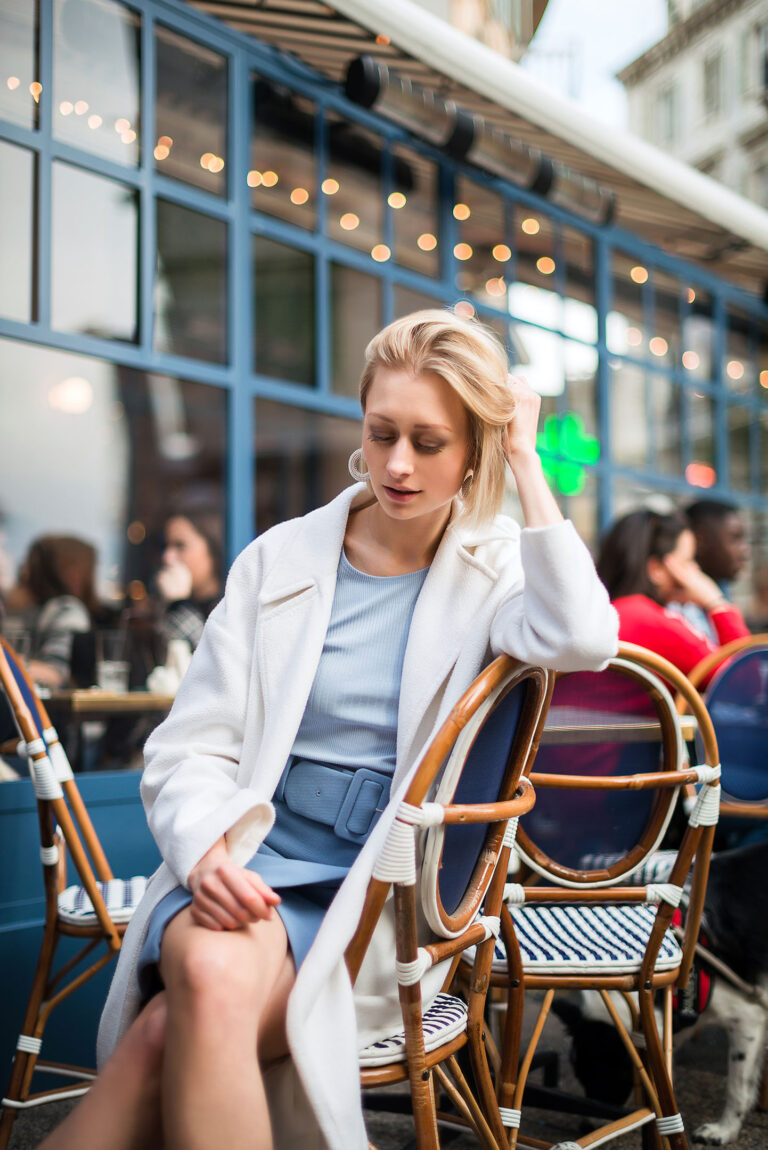Photographe portrait artistique à Nice : portrait d’une femme élégante attablée dans un café vitré, ambiance printanière.