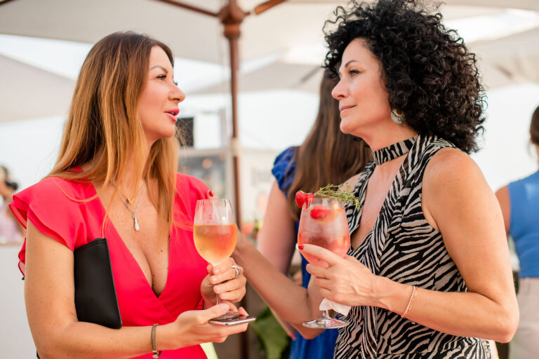 Échange complice entre deux femmes, cocktails à la main, dans une ambiance détendue.