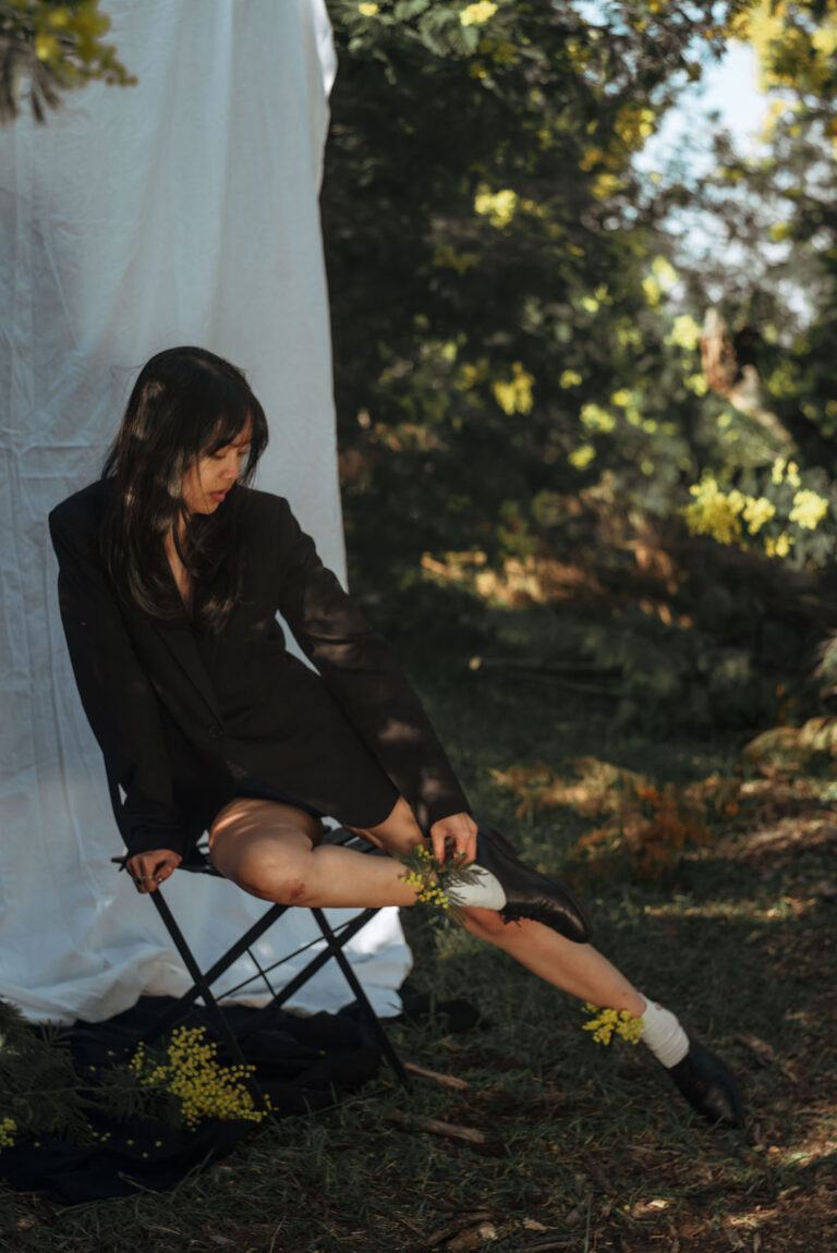 Justine, debout en veste ouverte, photographiée sur fond blanc au milieu de la nature.