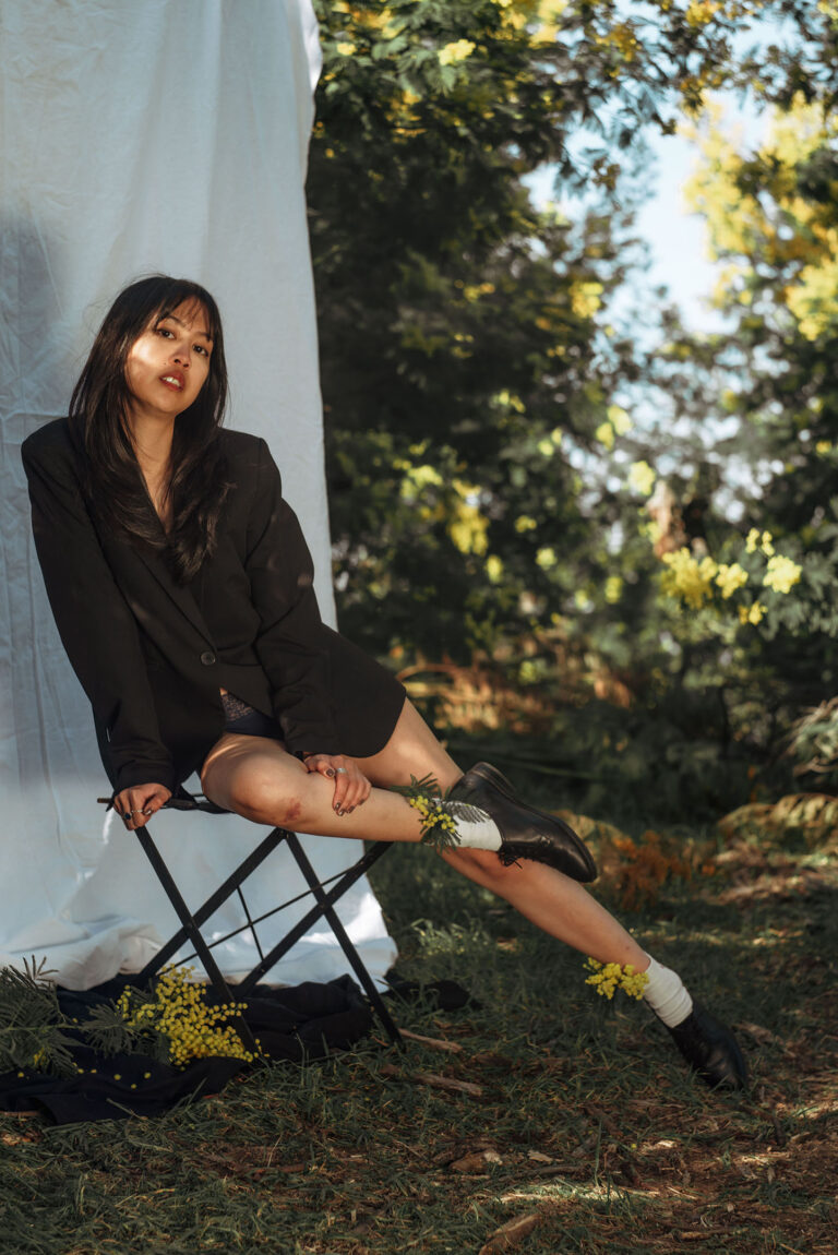 Séance photo audacieuse dans les mimosas : modèle en veste noire sur fond naturel contrasté.