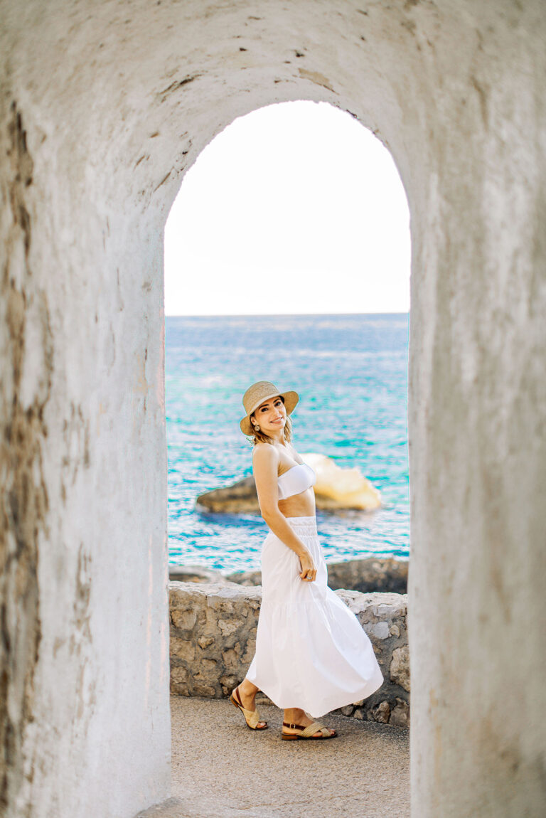 Cliché naturel d’une femme posant face à la mer en tenue blanche estivale.
