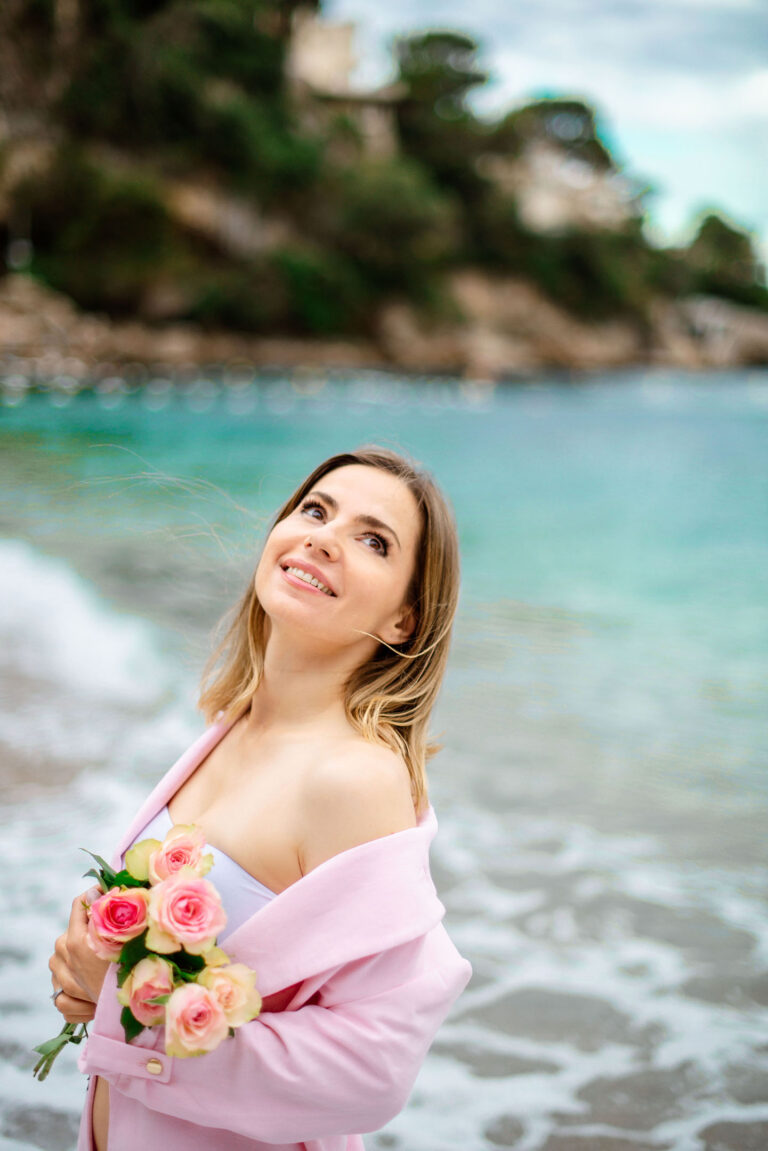 Femme posant en tenue rose avec fleurs sur fond de mer, plage de Cap d’Ail.