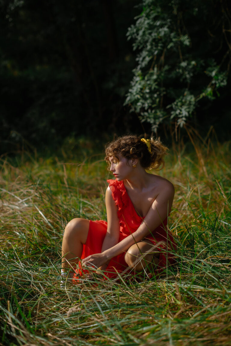 La robe écarlate de Silvia illumine la scène, assise en pleine nature – Photographe portrait nature Cannes.