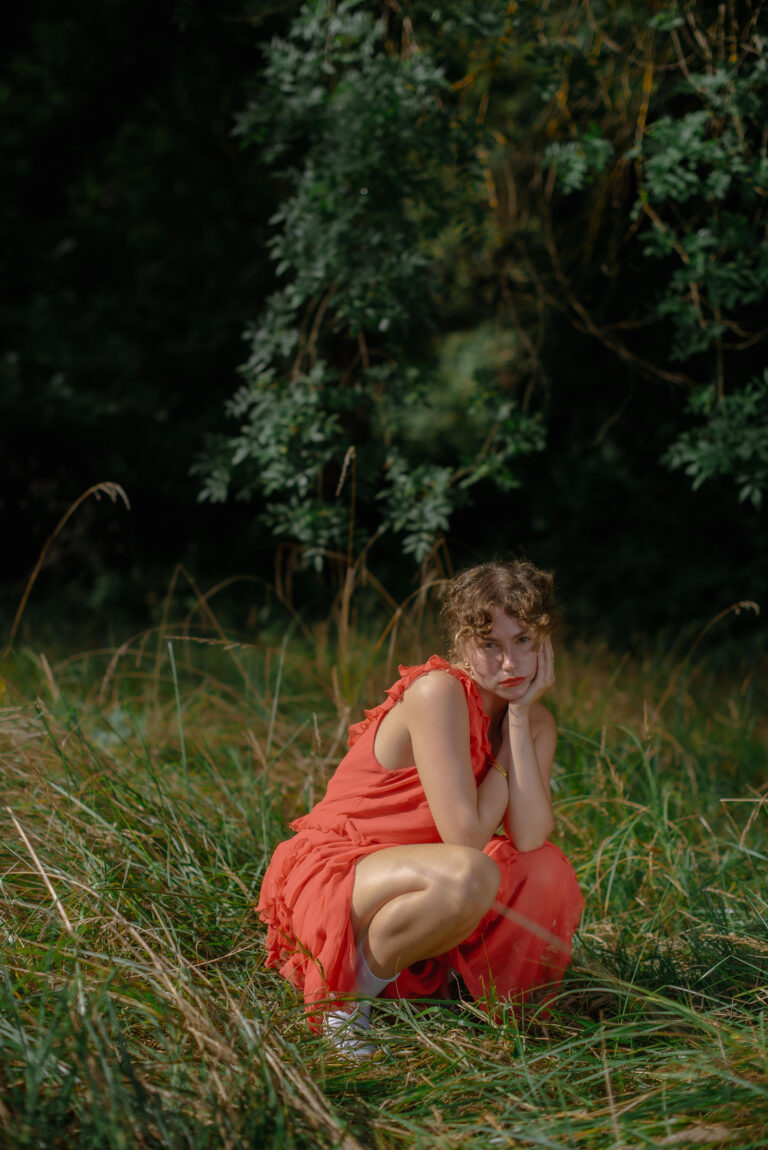 Un instant suspendu, Silvia songeuse, assise au cœur d’un écrin de verdure – Portrait poétique en extérieur.