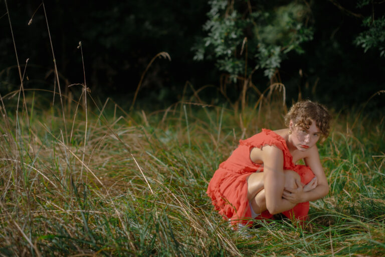 Silvia assise dans l’herbe, robe rouge contrastant avec le vert éclatant – Photographe portrait expressif Côte d’Azur.