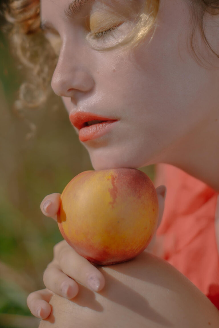 Portrait artistique sur la Côte d’Azur : lèvres rougeoyantes contre le fruit défendu, un geste empreint de liberté.