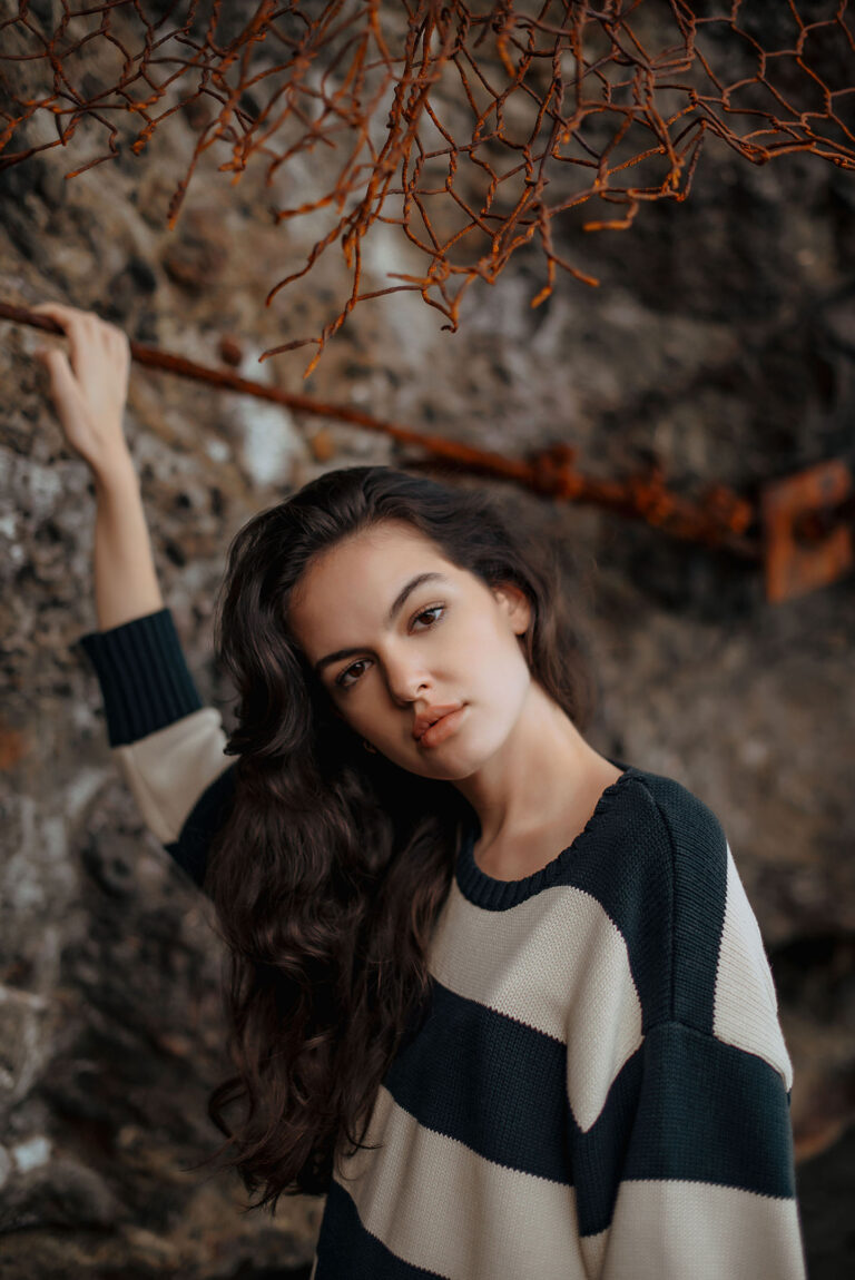 Portrait artistique de Sofia devant une grille métallique, mer en arrière-plan – photographe à Cap d’Ail.