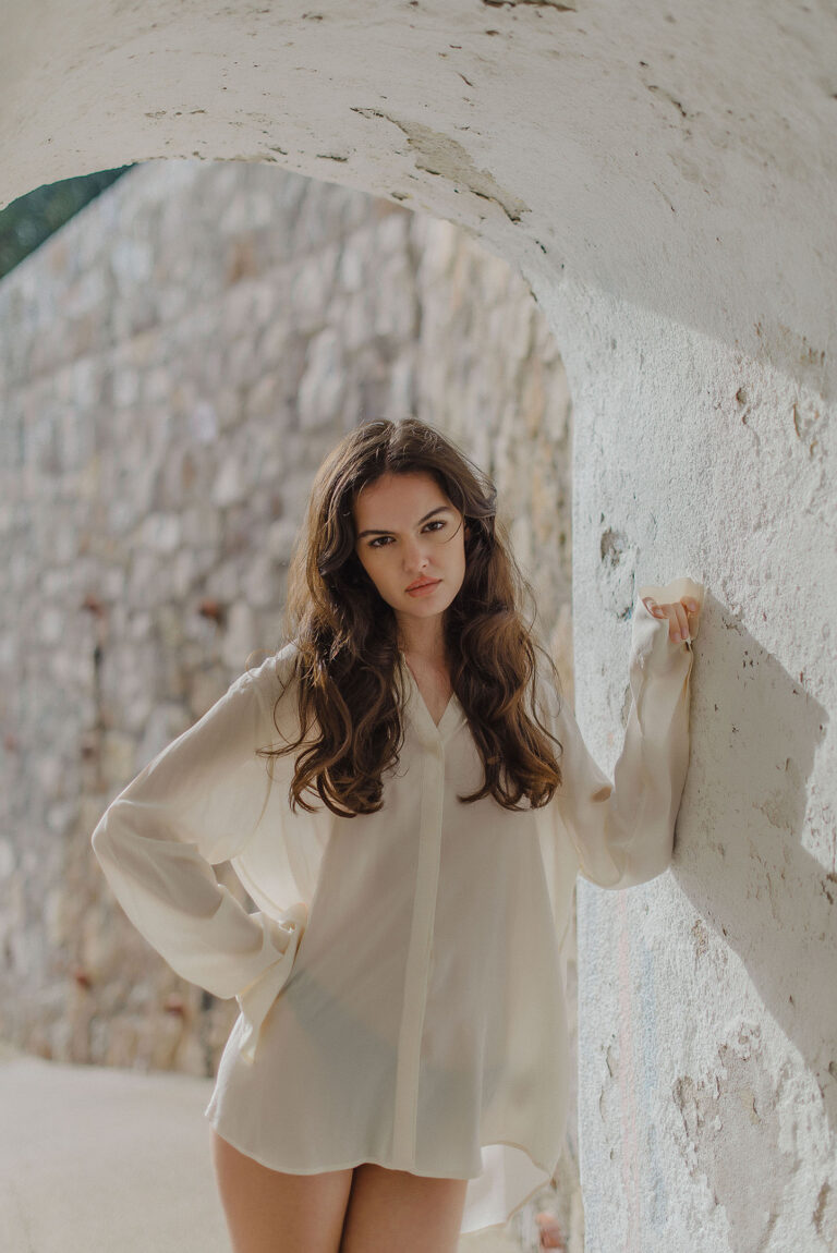 Photographe portrait à Cap d’Ail – modèle posant sous une arche blanche naturelle.