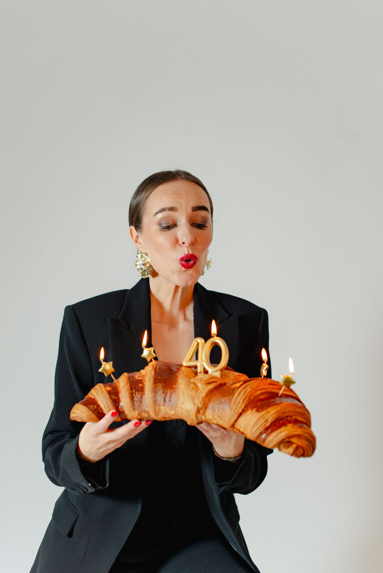 Portrait pétillant d'une femme soufflant ses bougies avec un croissant XXL.