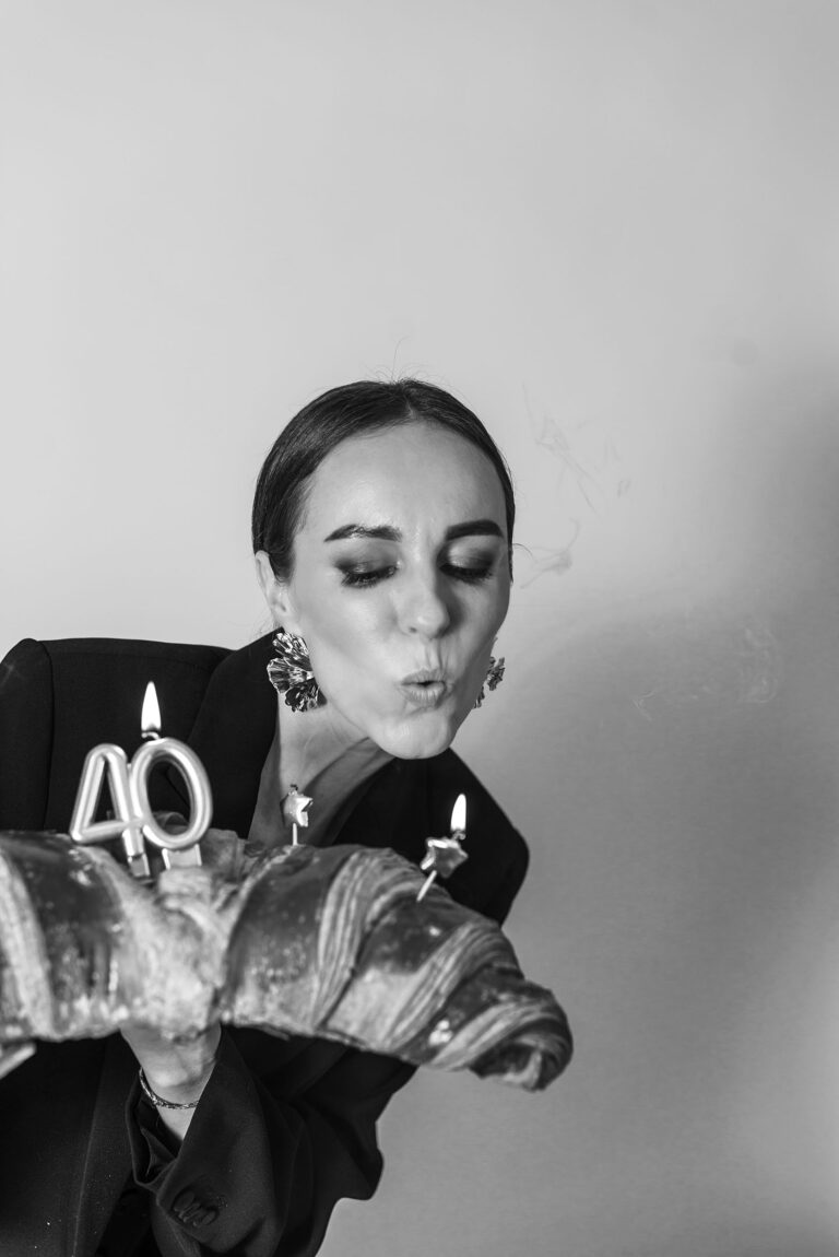 Portrait expressif d'une femme soufflant ses bougies sur un croissant géant.