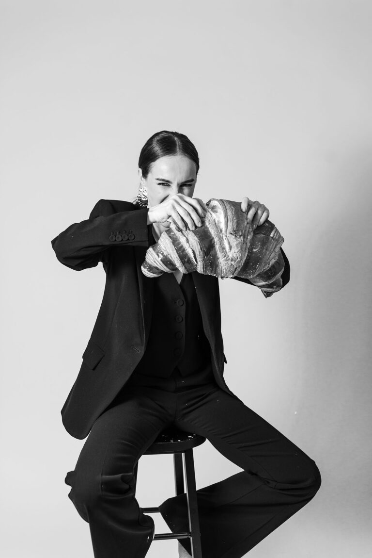 Photo humoristique en studio : femme déchirant un croissant géant avec énergie.