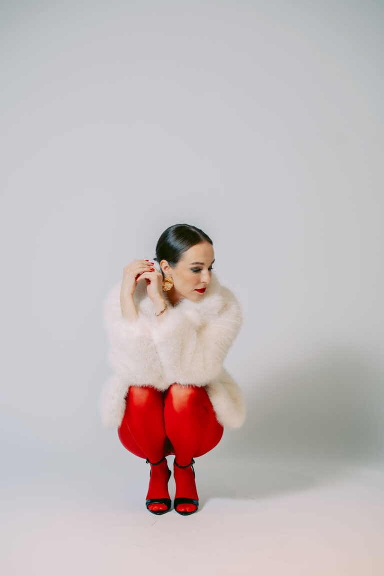 Photo glamour d’une femme en collants rouges et manteau blanc lors d’un shooting en studio.